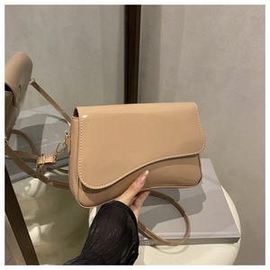 Close-up of beige patent leather shoulder bag with unique asymmetric wavy flap design