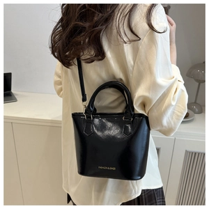 Vue détaillée du sac seau en cuir verni noir avec lettrage doré et fine bandoulière réglable