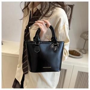 Detail of black glossy PU bucket bag with gold lettering and sturdy dual top handles