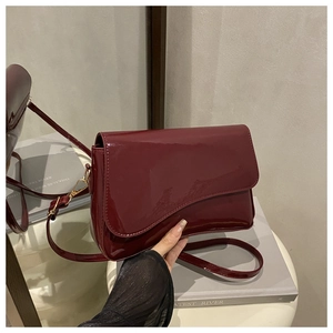 Detail of burgundy patent leather handbag featuring wavy flap design and gold hardware