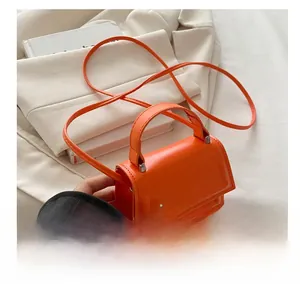 Detail of bright orange mini square bag with glossy leather texture and rounded handle