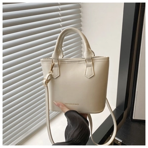 Detailed view of cream-white leather bucket bag with dual handles and gold-tone lettering