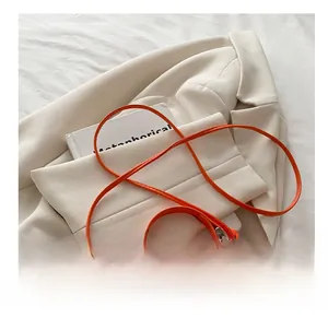 Detail of a bright orange mini crossbody bag on a white suit with slim shoulder strap