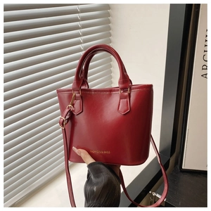 Close-up of a glossy red bucket bag with metallic strap and fashion brand logo detail