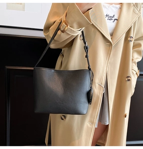 Close-up of black lychee grain leather shoulder bag with adjustable strap on a beige coat