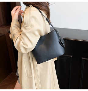 Detail of black lychee grain leather bucket bag with knot decoration on beige coat