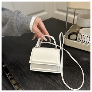 Detail shot of white mini leather crossbody bag with top handle and stitched flap closure