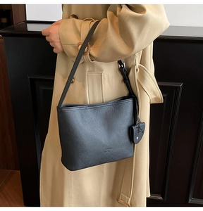 Detail of black pebble leather shoulder bag with heart charm on a trench coat model