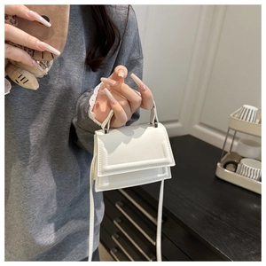 Close-up of white mini handbag with handle and crossbody strap being held in hand