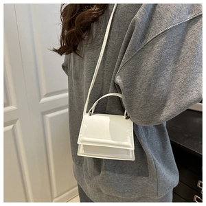 Minimalist white mini crossbody bag worn on shoulder over a casual grey sweatshirt