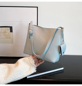 Detail of light blue bucket bag in lychee leather with side charm and adjustable strap