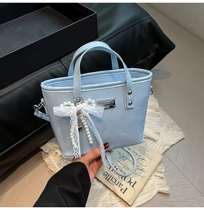 Detail of light blue patent leather bucket bag with lace bow and pearl charm