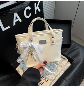Detail of cream bucket bag with lace pearl bow charm and metal logo plaque in lifestyle setting