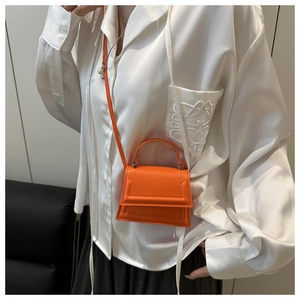 Close-up of a bright orange mini square bag with top handle and slender crossbody strap