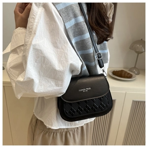 Detail of black crossbody bag with quilted stitching and gold fashion lettering on flap