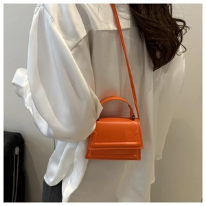 Back view of a model wearing a mini orange leather crossbody bag on a white silk shirt