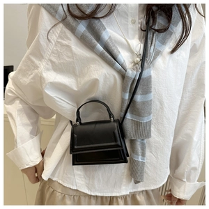 Close-up of a minimalist black leather crossbody bag worn by a model in a white shirt