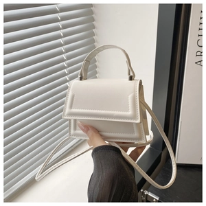 Detail of a white minimalist crossbody bag with textured stitching and silver hardware