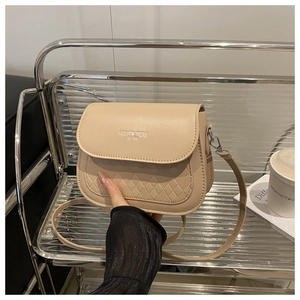 Close-up of beige saddle bag featuring woven texture stitching and gold logo details