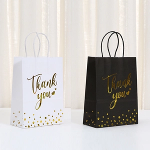 Detalle de bolsas de regalo en blanco y negro con texto dorado y asas trenzadas