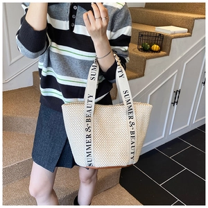Detail of hand-woven beige straw tote bag with printed SUMMER & BEAUTY webbing handles