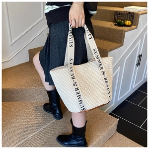 Detailed shot of beige straw tote bag with lettered straps and brown leather base