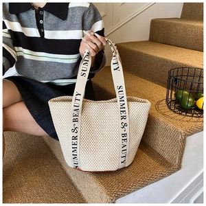 Detail view of woven straw tote bag featuring Summer & Beauty printed handle straps