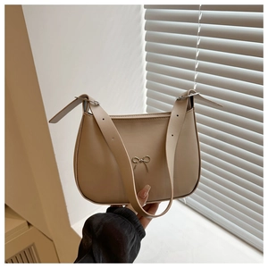 Detail of a beige half-moon shoulder bag with a small metallic bow and wide strap