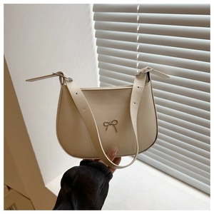 Detail of beige crescent shoulder bag featuring a decorative silver metallic bow accent
