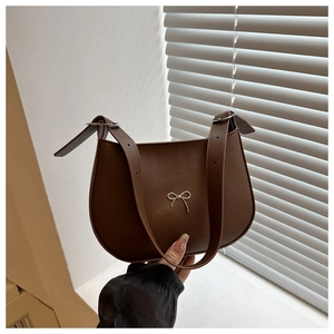 Detail of dark brown crescent underarm bag with gold metal bow and adjustable strap