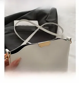 Detailed close-up of golden metal buckle on a white leather shoulder bag for women