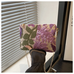 Close-up of beige woven clutch with purple sequin flowers and green leaf embroidery