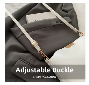 Close-up of adjustable golden buckle on white minimalist crossbody bag over grey suit