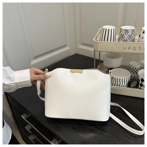Detail of a minimalist white crossbody bag with gold hardware on a dark wooden table