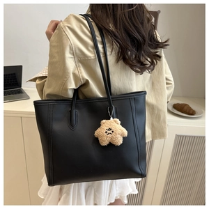 Detail of a black leather tote bag with long shoulder strap and cute plush charm accessory