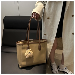 Detail of khaki tote bag with dark brown handles and a cute plush bear charm