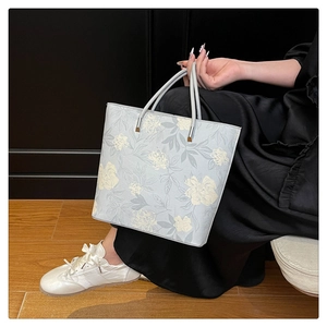 Close-up of light blue floral tote bag with grey handles and elegant silver hardware