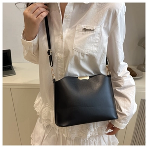 Detail view of black bucket bag with golden metal trim and adjustable strap on a model