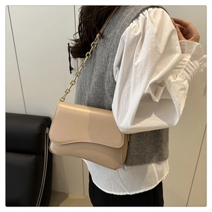 Dettaglio di una borsa a tracolla beige con catena dorata indossata con un outfit elegante
