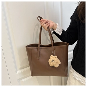 Detail of a brown leather tote bag with a cute plush bear charm in a lifestyle setting