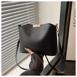 Detail of black leather handbag featuring curved gold metal hardware and slim strap