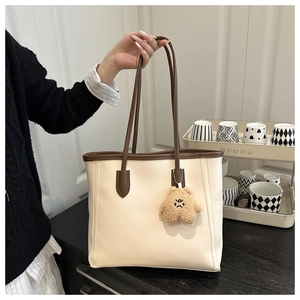 Detail of a minimalist cream tote bag with brown handles and a plush bear charm