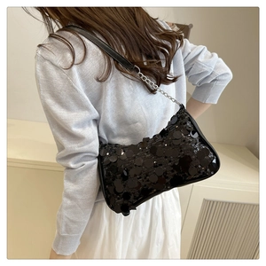 Detail of black sequin underarm bag with metal chain strap on a model's shoulder