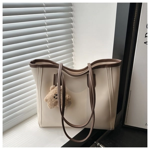 Detail of a chic cream tote bag with brown trim and a plush teddy bear charm accessory