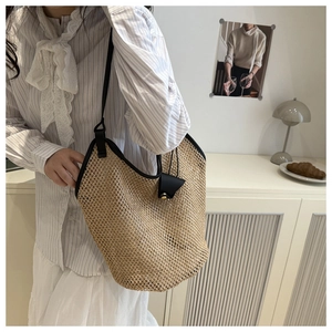 Detail of woven straw tote bag with black leather trim and metal lock in a lifestyle setting