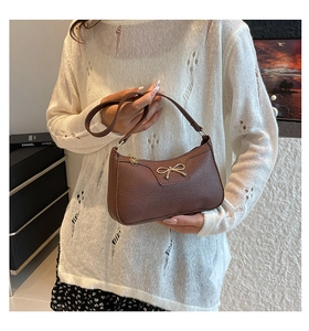 Close-up of deep brown lychee texture leather bag with a golden metal bow detail