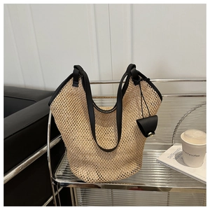 Detail of woven straw tote bag with black slim straps and a mini leather pouch accessory