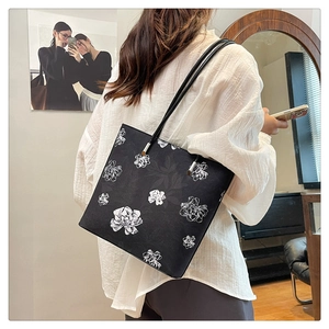 Detail of black tote bag with white floral pattern and silver hardware on a shoulder strap