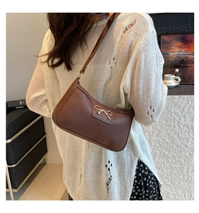 Detailed close-up of dark brown lychee pattern leather shoulder bag with golden bow