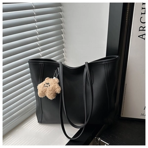 Detail of black matte leather tote bag with long straps and plush bear charm